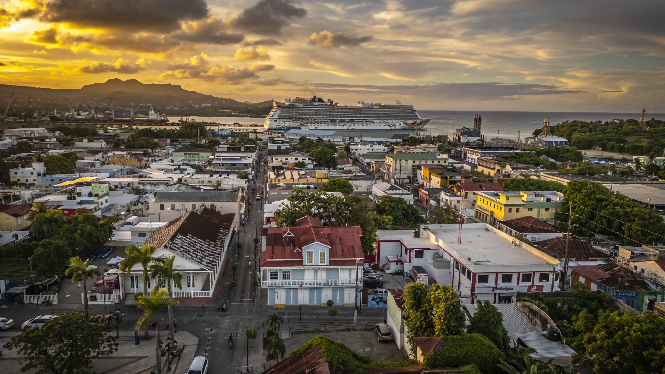 buyDRproperty Puerto Plata cityscape at sunset with cruise ship in background. Colorful buildings and coastline view. Sosua Real Estate