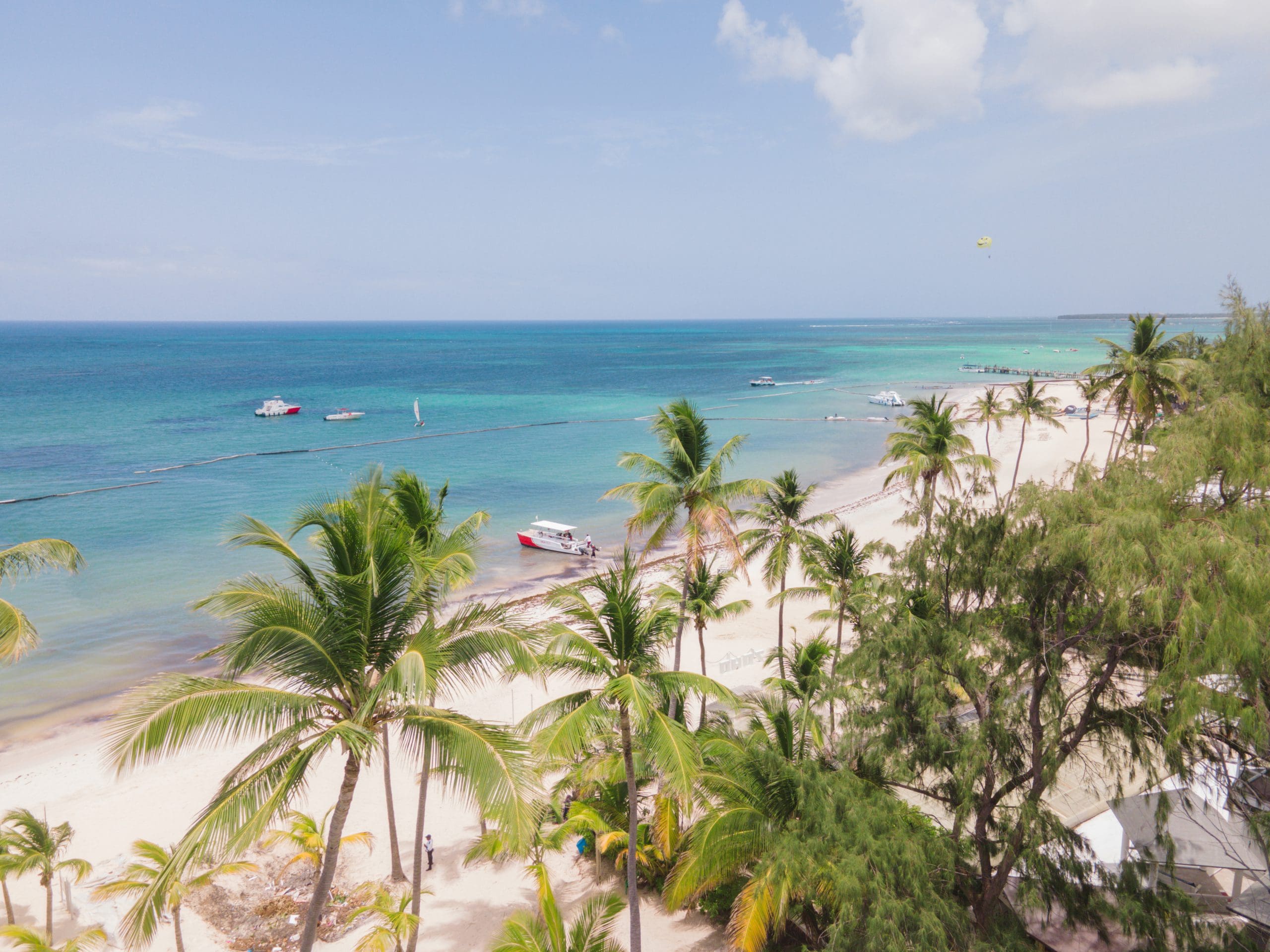 buyDRproperty Tropical beach scene with palm trees, white sand, turquoise water, and boats under a sunny sky. Sosua Real Estate