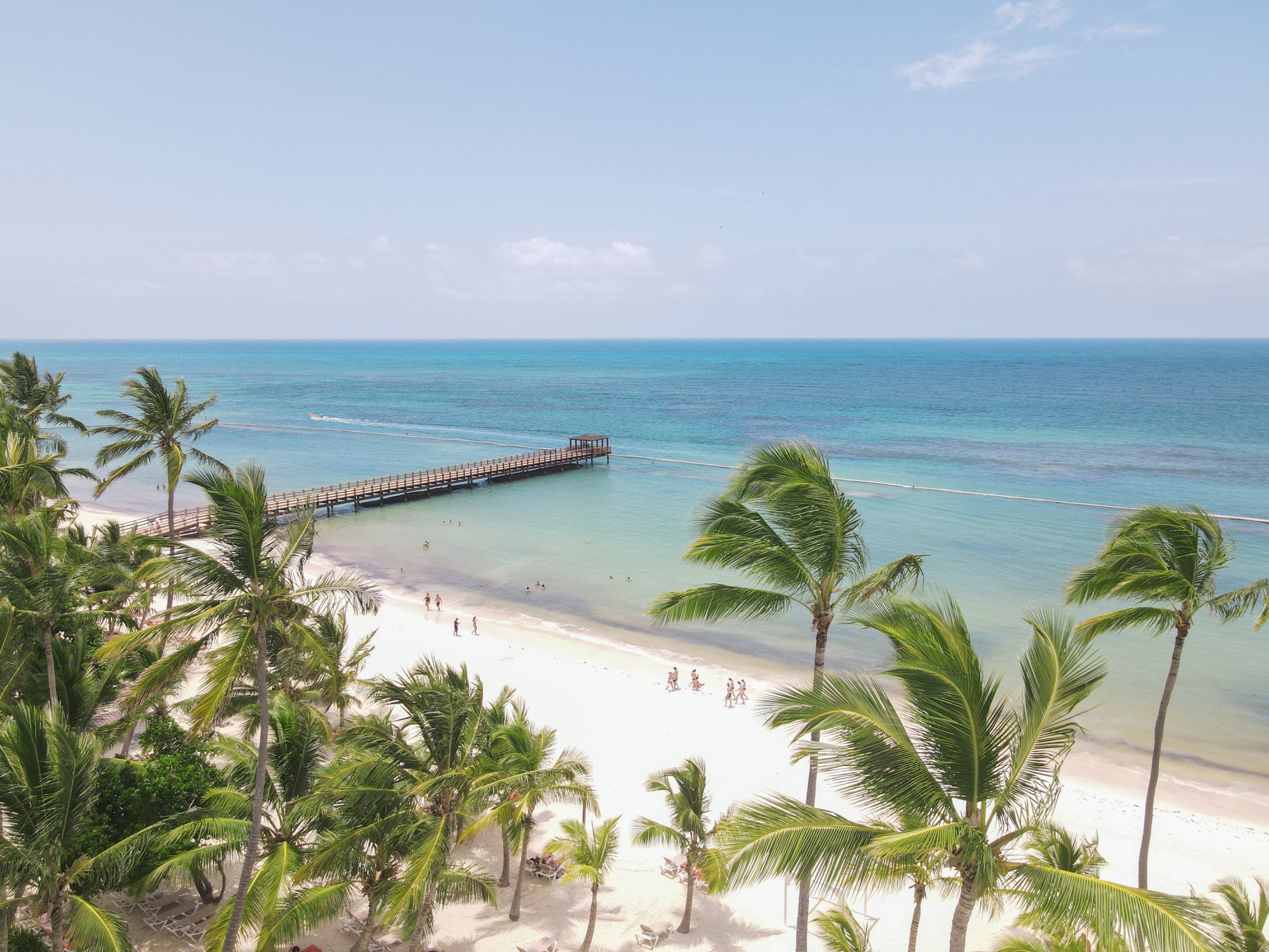 buyDRproperty Palm trees line a white sand beach with a pier extending into turquoise water. Sosua Real Estate