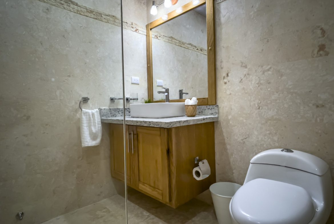 buyDRproperty Bathroom with modern sink, toilet, granite countertop, wood cabinet, and neutral tile walls. Sosua Real Estate