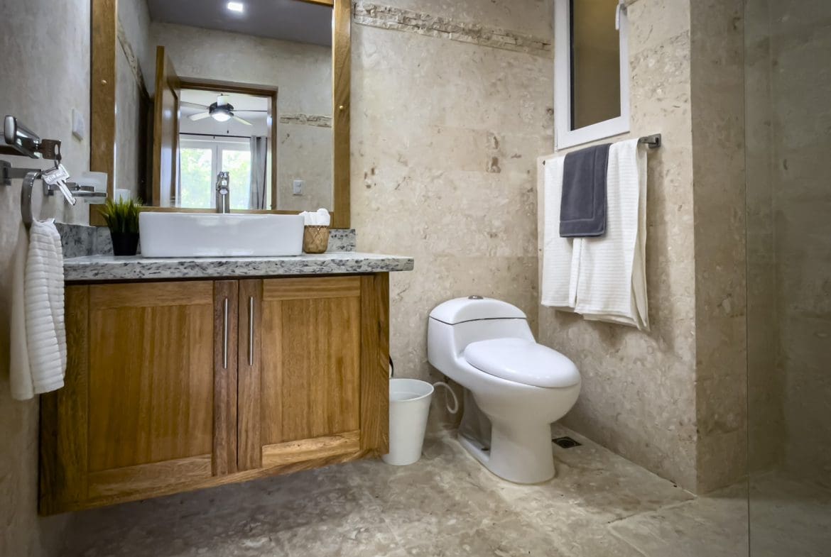 buyDRproperty Bathroom featuring wood cabinet, modern toilet, marble walls, and a large mirror. Sosua Real Estate