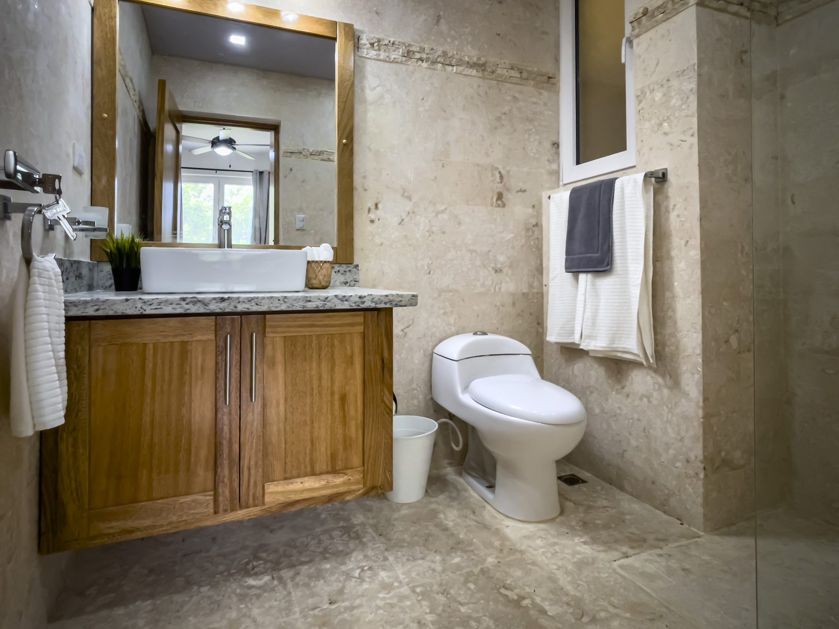 buyDRproperty Bathroom featuring wood cabinet, modern toilet, marble walls, and a large mirror. Sosua Real Estate