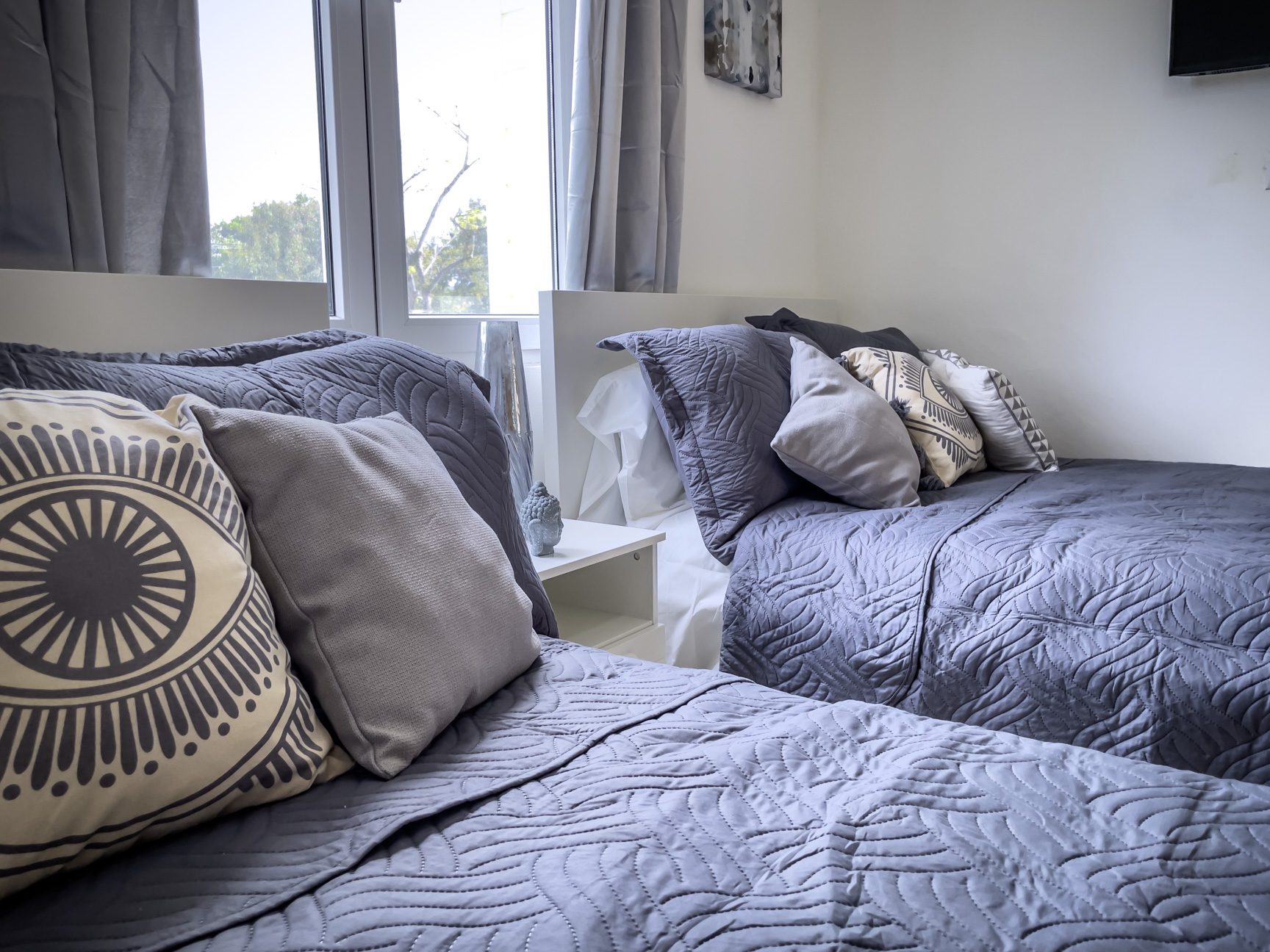 buyDRproperty Two twin beds with grey quilts and decorative pillows, bright window. Sosua Real Estate