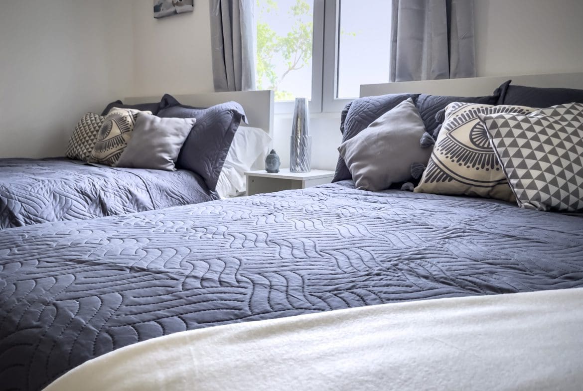 buyDRproperty Two beds in a bright bedroom with grey bedding and decorative pillows. Sosua Real Estate