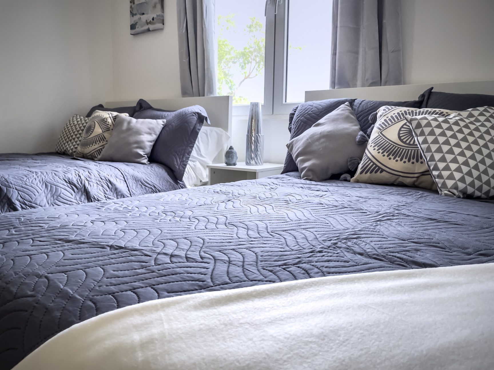 buyDRproperty Two beds in a bright bedroom with grey bedding and decorative pillows. Sosua Real Estate