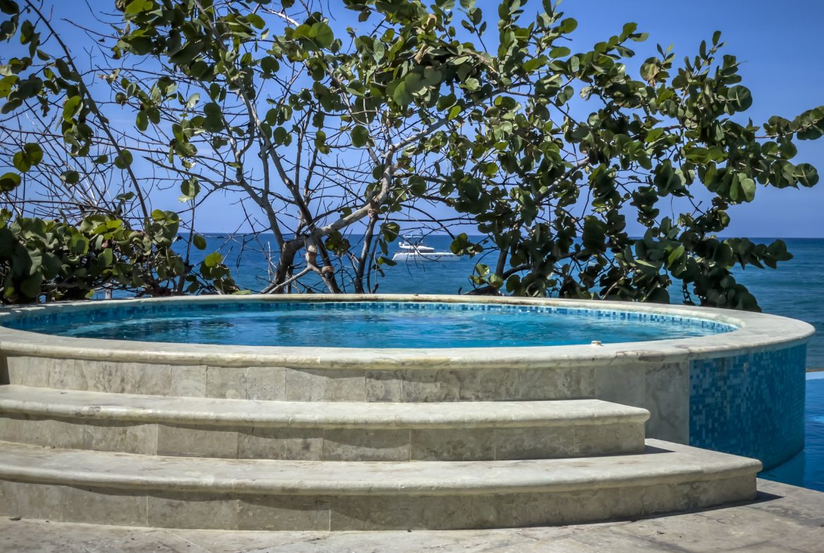 buyDRproperty Caribbean vacation pool with ocean view, lush greenery, and a yacht in the distance Sosua Real Estate