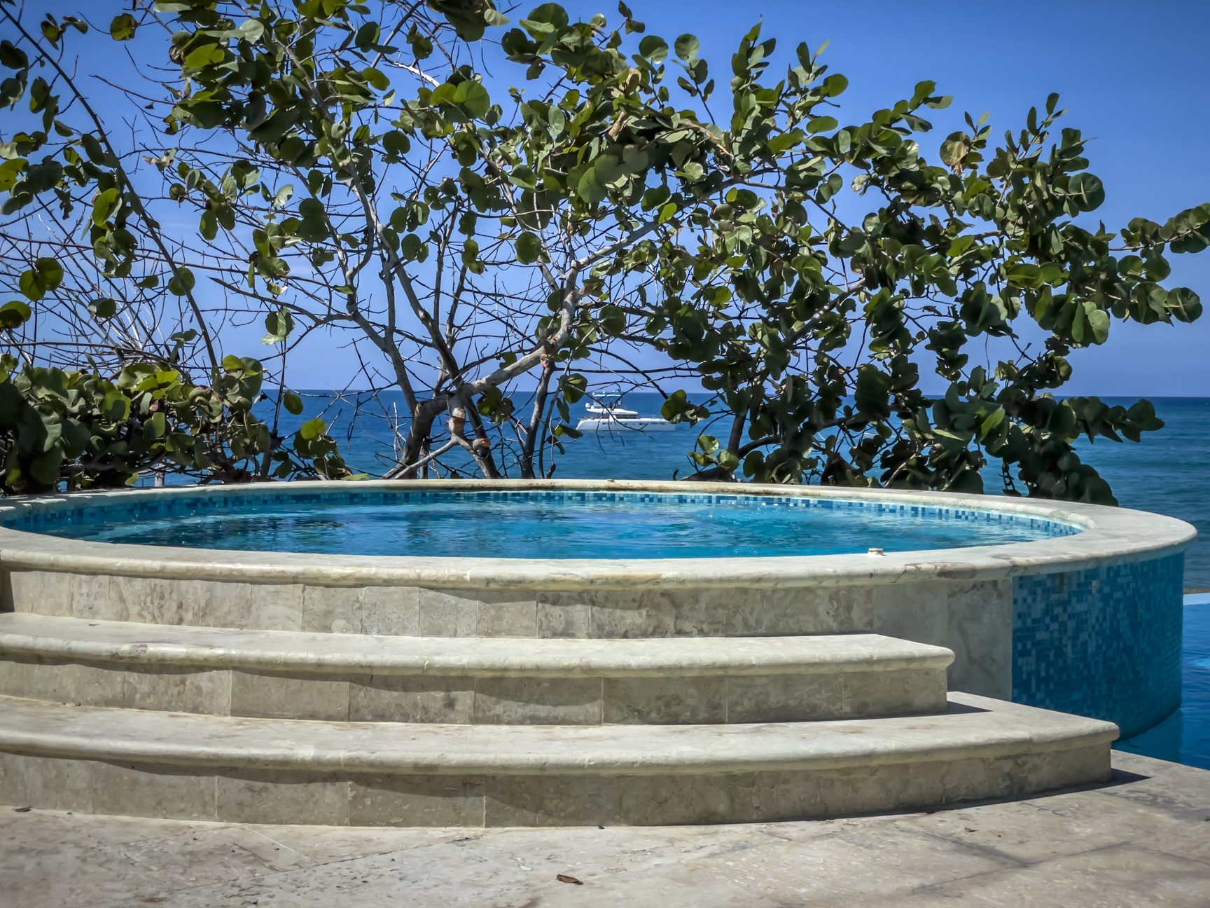 buyDRproperty Caribbean vacation pool with ocean view, lush greenery, and a yacht in the distance Sosua Real Estate