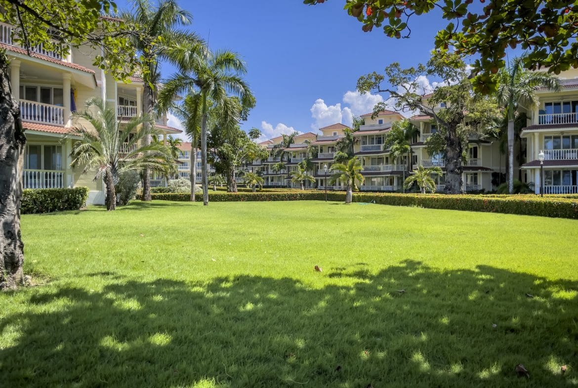 buyDRproperty Lush green lawn with palm trees between resort buildings under a clear blue sky. Sosua Real Estate