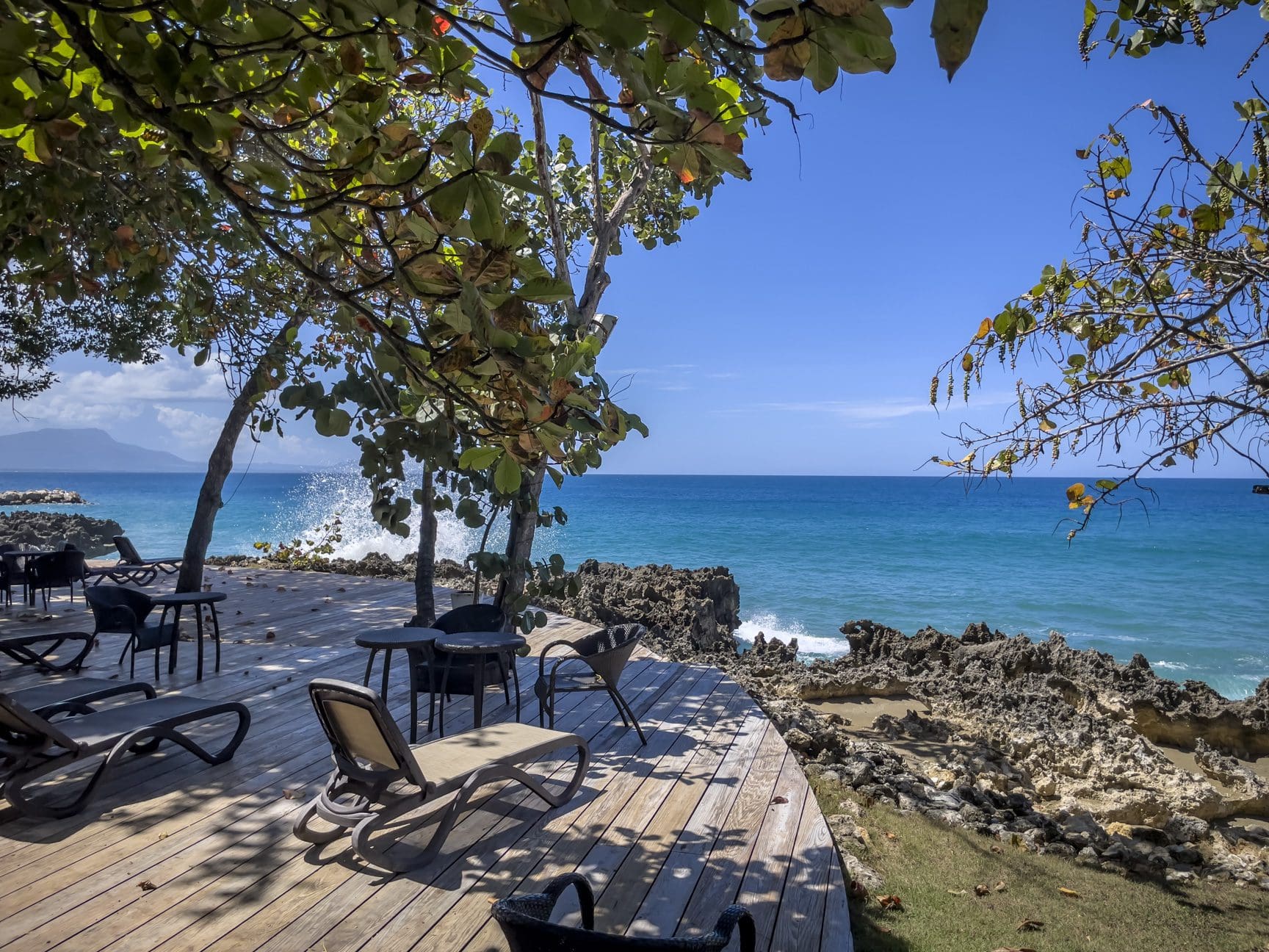 buyDRproperty Wooden deck with lounge chairs overlooking a turquoise ocean and rocky coastline under a clear blue sky. Sosua Real Estate