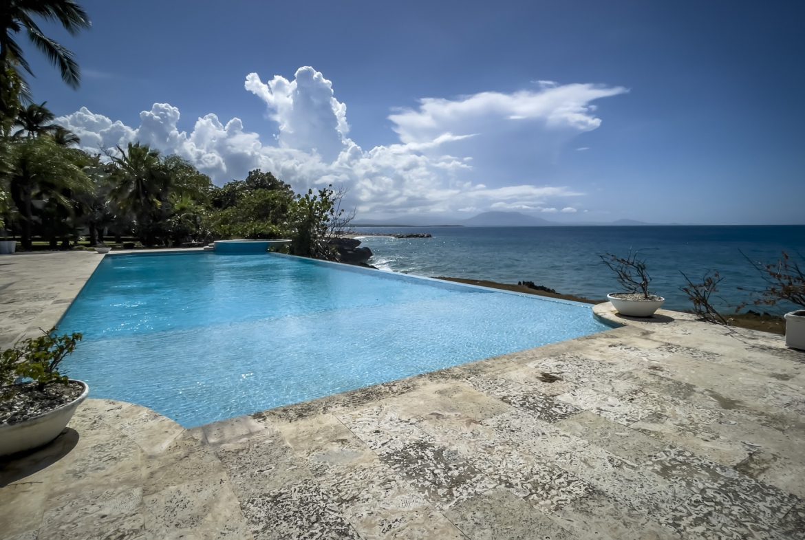 buyDRproperty Infinity pool overlooking the turquoise ocean under a partly cloudy blue sky Sosua Real Estate