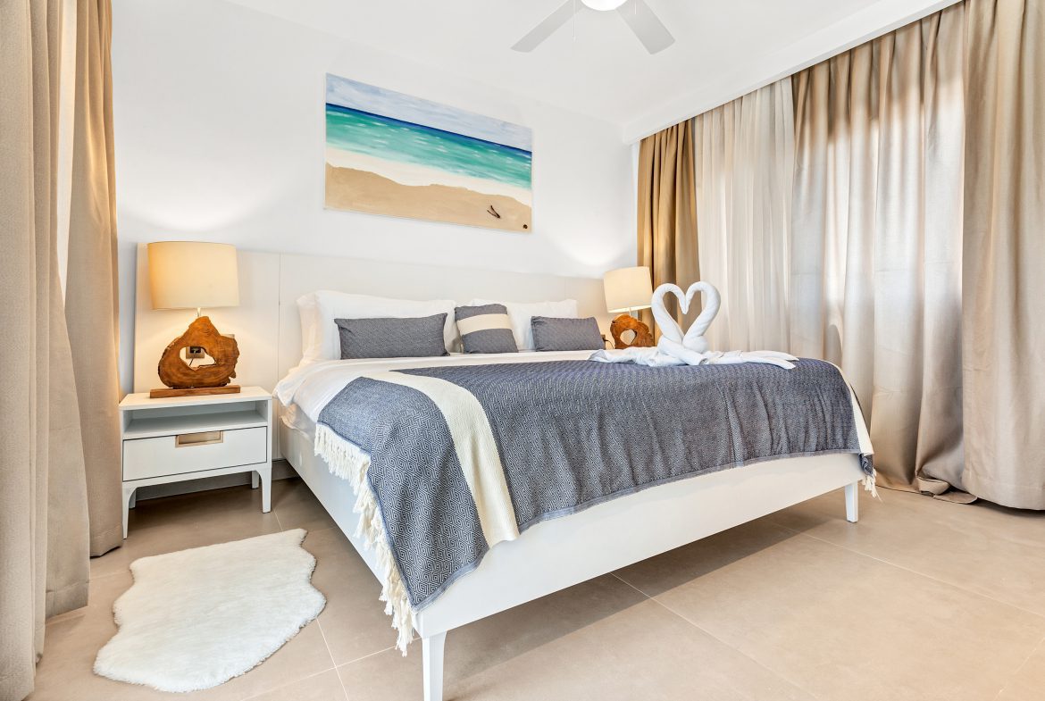 buyDRproperty White bedroom with blue accents, beach art, and decorative towel swans. Sosua Real Estate