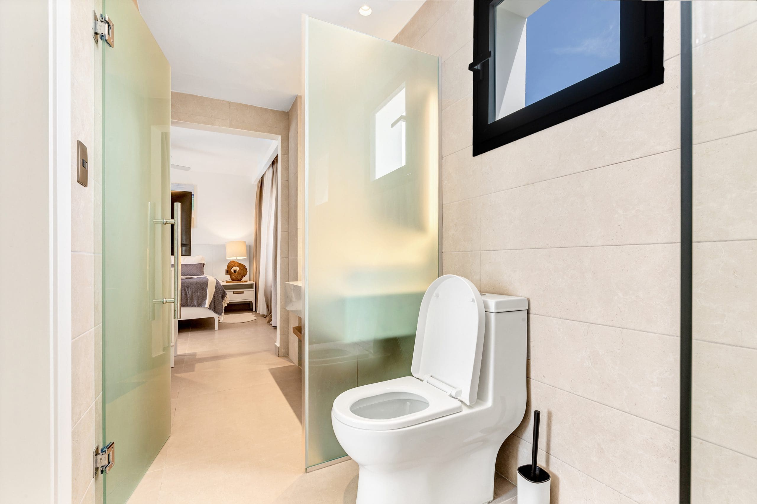 buyDRproperty Modern bathroom with white toilet, frosted glass partition, and bedroom view. Sosua Real Estate