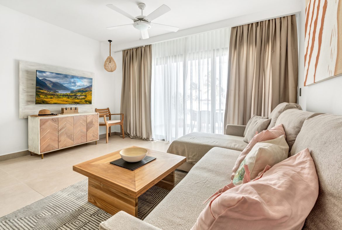 buyDRproperty Bright living room with a sectional sofa, wooden coffee table, and TV. Neutral tones and natural light. Sosua Real Estate