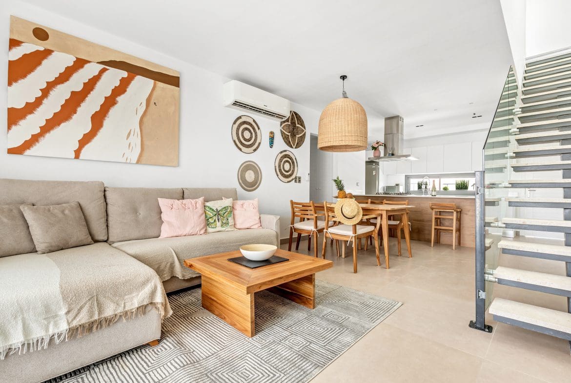 buyDRproperty Bright, modern living room with sofa, dining table, and open kitchen. Neutral tones and natural textures create a relaxed atmosphere. Sosua Real Estate