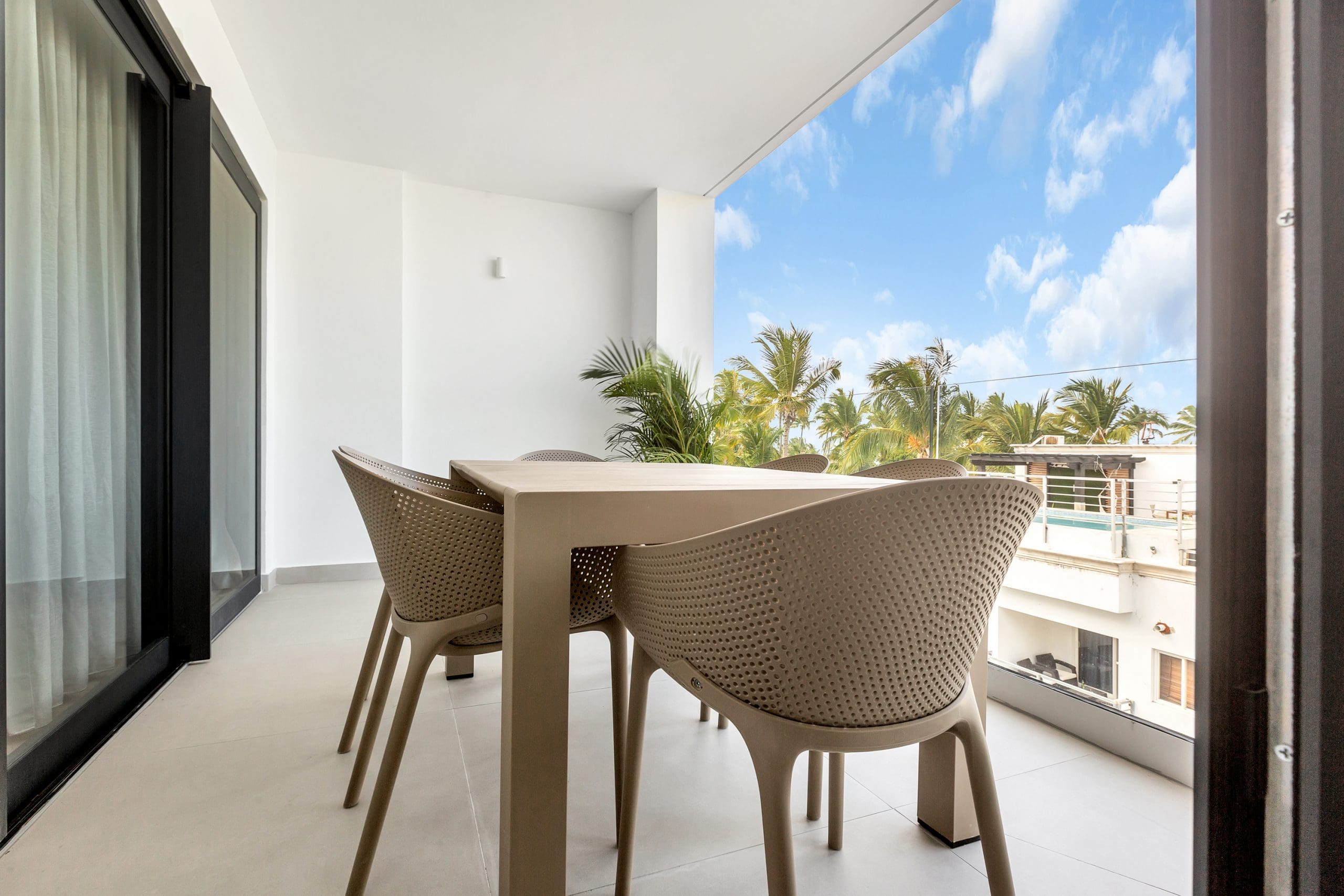 buyDRproperty Balcony with table and chairs overlooking tropical trees and a building with a pool. Sosua Real Estate