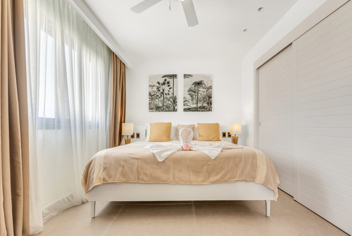 buyDRproperty Bright bedroom featuring a king-size bed with swan towel art, neutral tones, and tropical wall art. Sosua Real Estate
