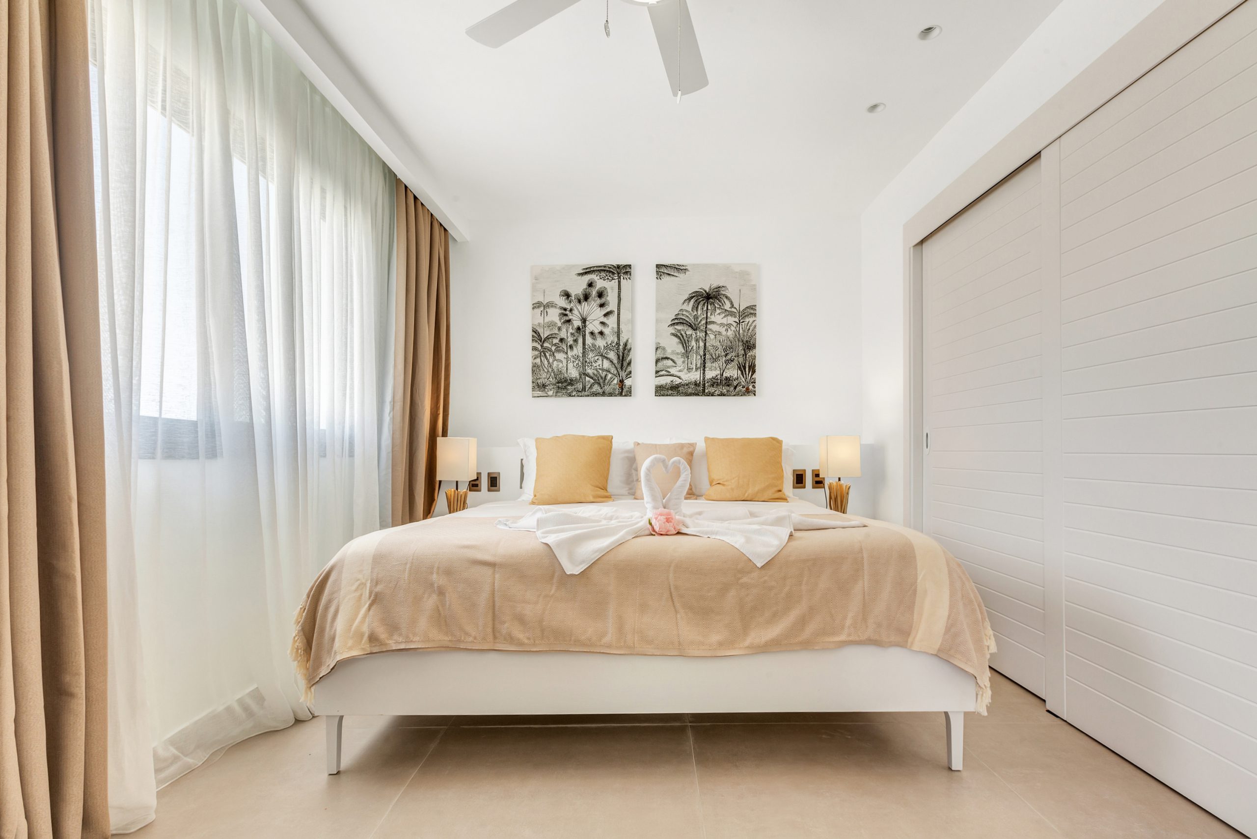 buyDRproperty Bright bedroom featuring a king-size bed with swan towel art, neutral tones, and tropical wall art. Sosua Real Estate