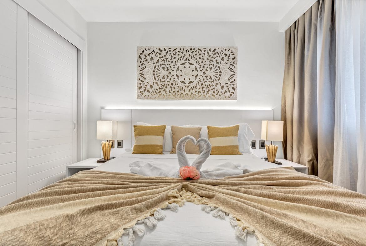 buyDRproperty Luxurious hotel bedroom with swan towel art, decorative headboard, and neutral color scheme. Sosua Real Estate