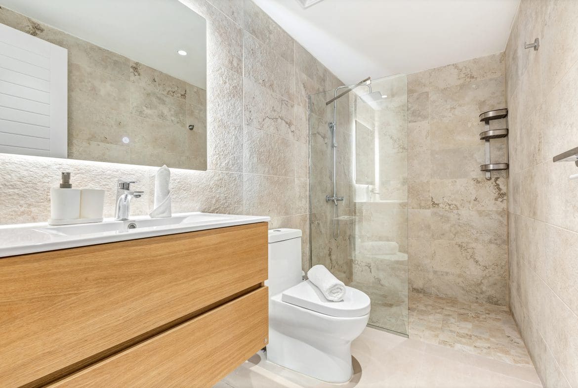 buyDRproperty Modern bathroom with wood vanity, toilet, and glass shower. Neutral tile and clean design. Sosua Real Estate
