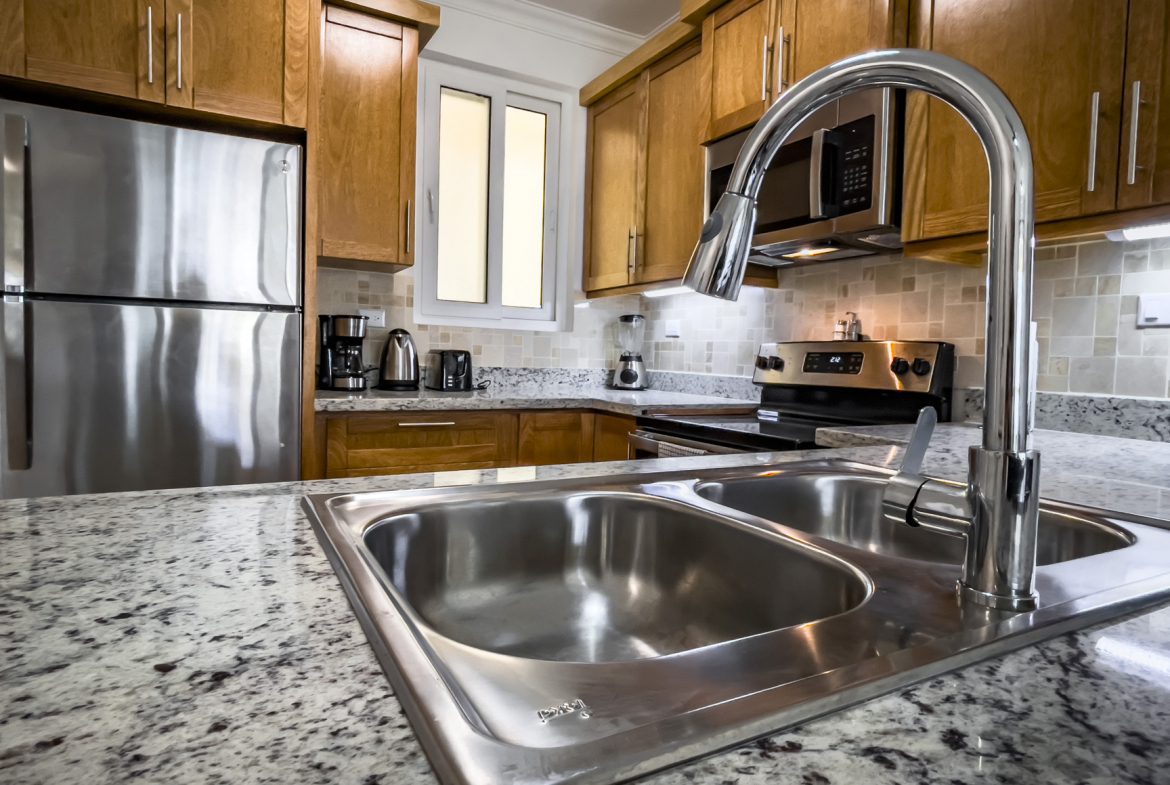 buyDRproperty Modern kitchen with stainless steel appliances, granite countertops, and a double basin sink. Sosua Real Estate