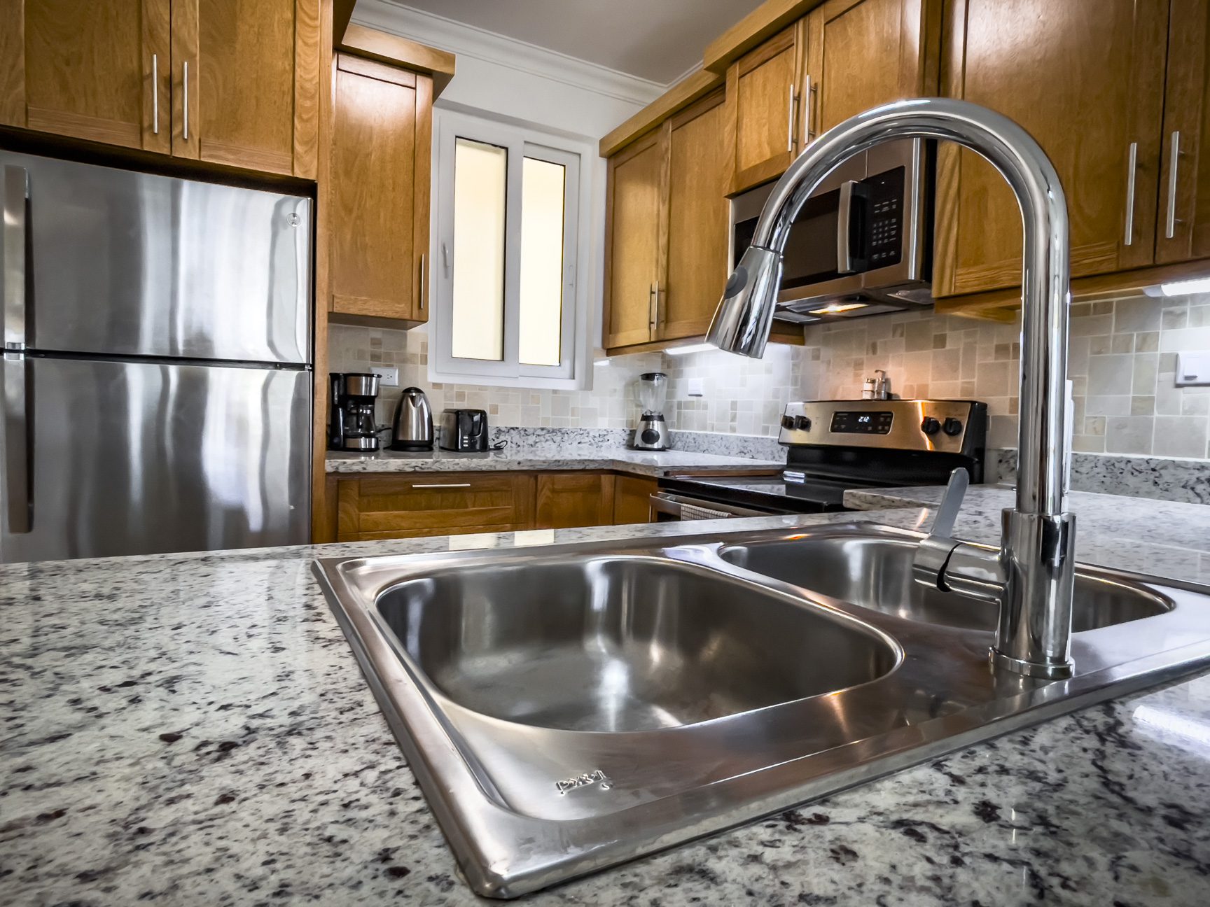 buyDRproperty Modern kitchen with stainless steel appliances, granite countertops, and a double basin sink. Sosua Real Estate