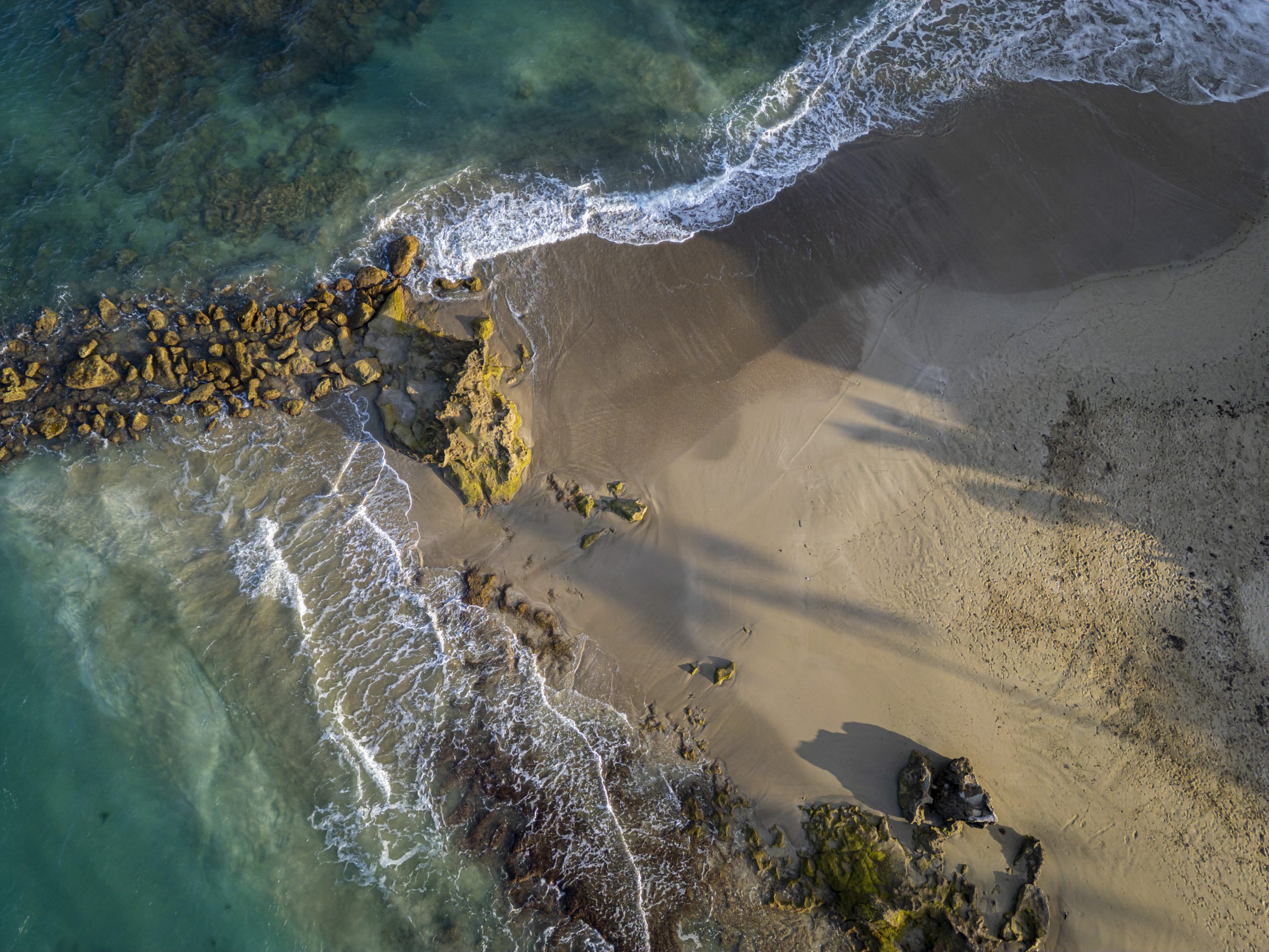 buyDRproperty Aerial view of a tropical beach with turquoise water, rocks, and sandy shore. Sosua Real Estate