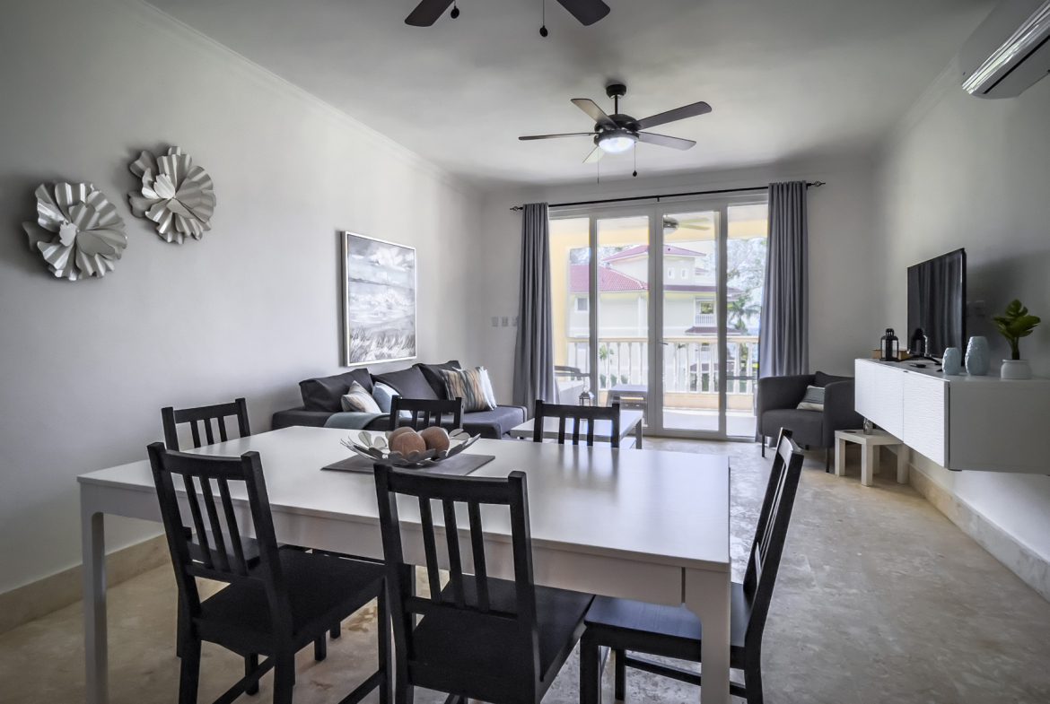 buyDRproperty Bright living room with white dining table, black chairs, and patio doors leading to a sunny outdoor area. Sosua Real Estate