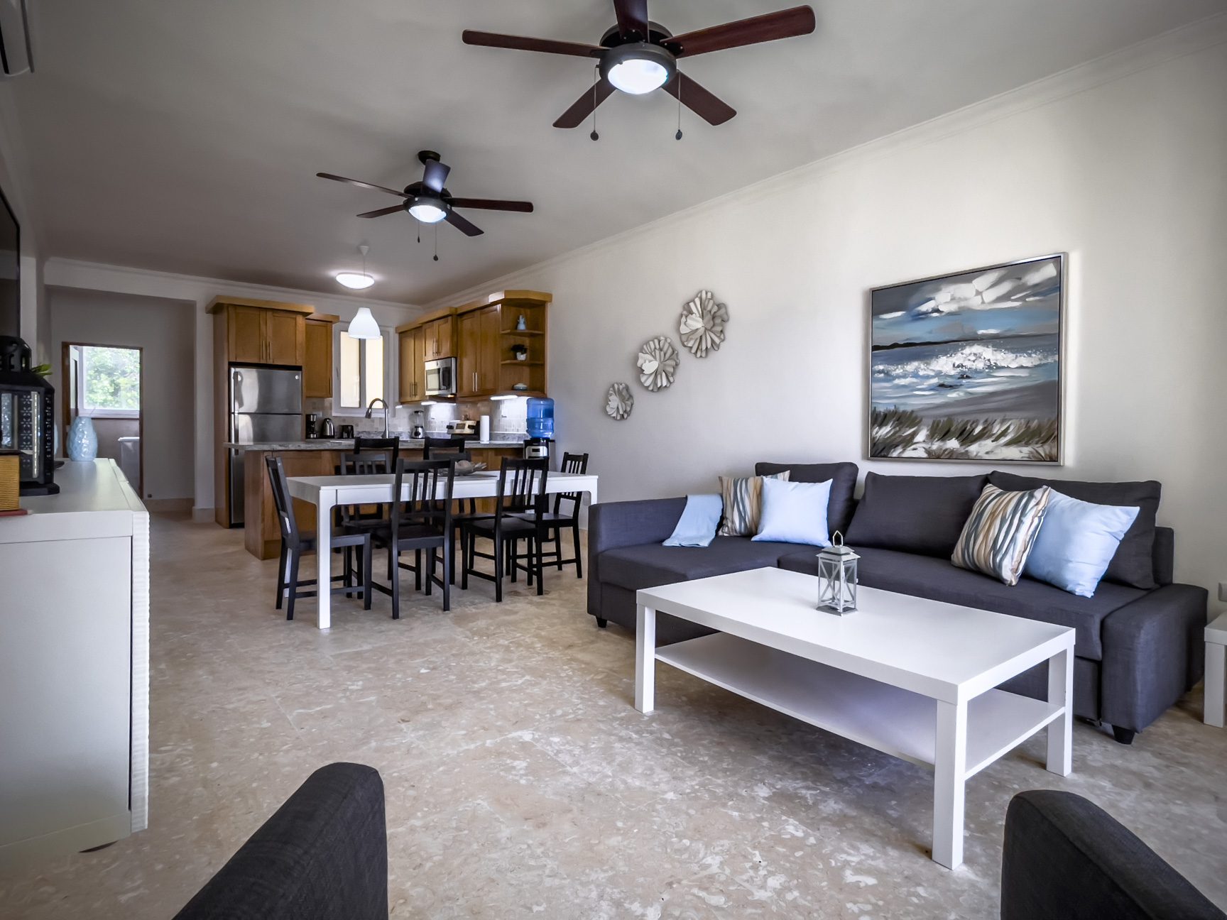 buyDRproperty Living room with gray sofa, white coffee table, dining area, and kitchen. Ceiling fans provide air circulation. Sosua Real Estate