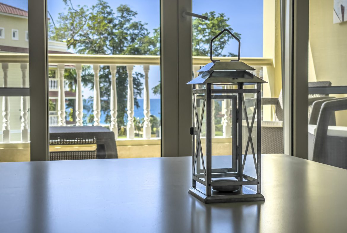 buyDRproperty Lantern on a table with balcony view of ocean and tropical trees. Sosua Real Estate