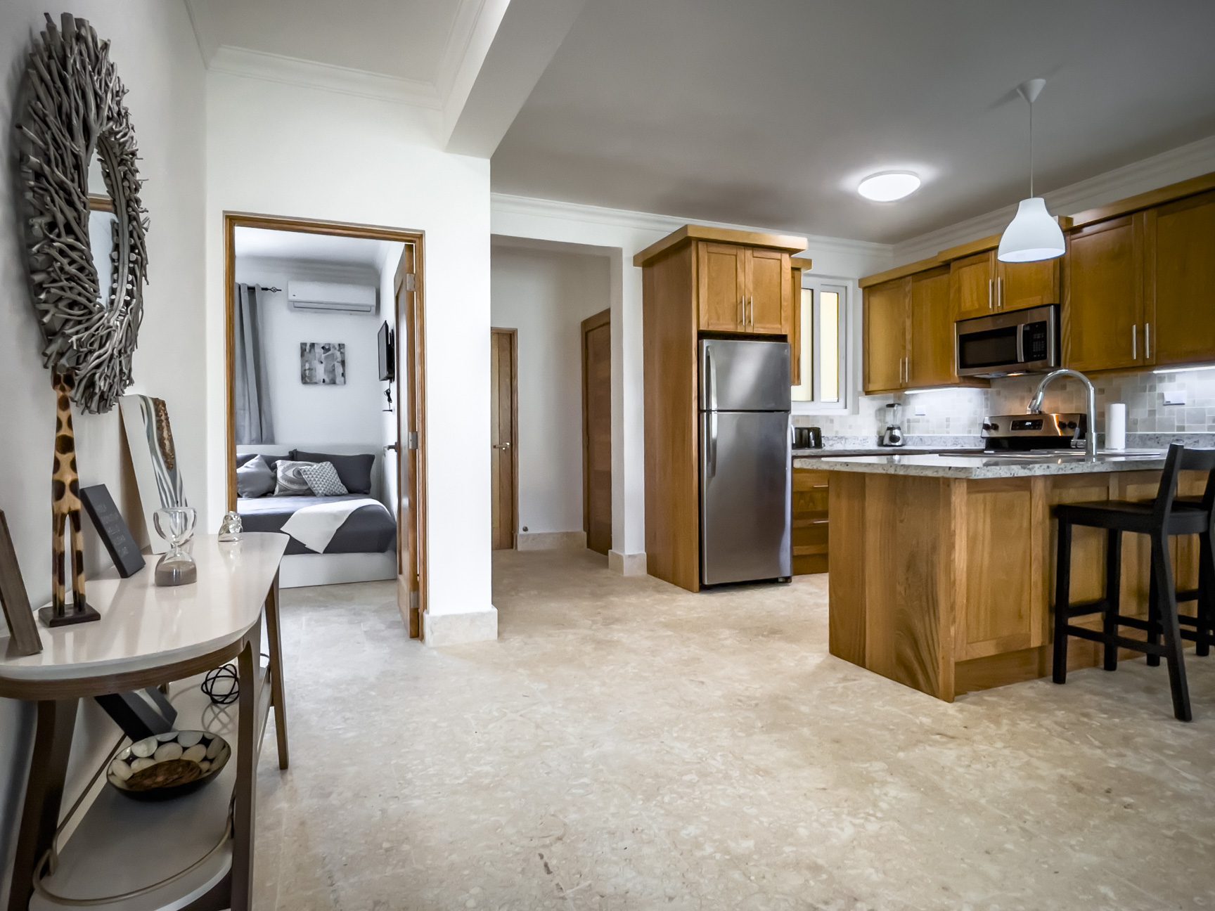 buyDRproperty Modern apartment interior with kitchen, bedroom, and decor. Neutral tones and wood finishes create a warm atmosphere. Sosua Real Estate