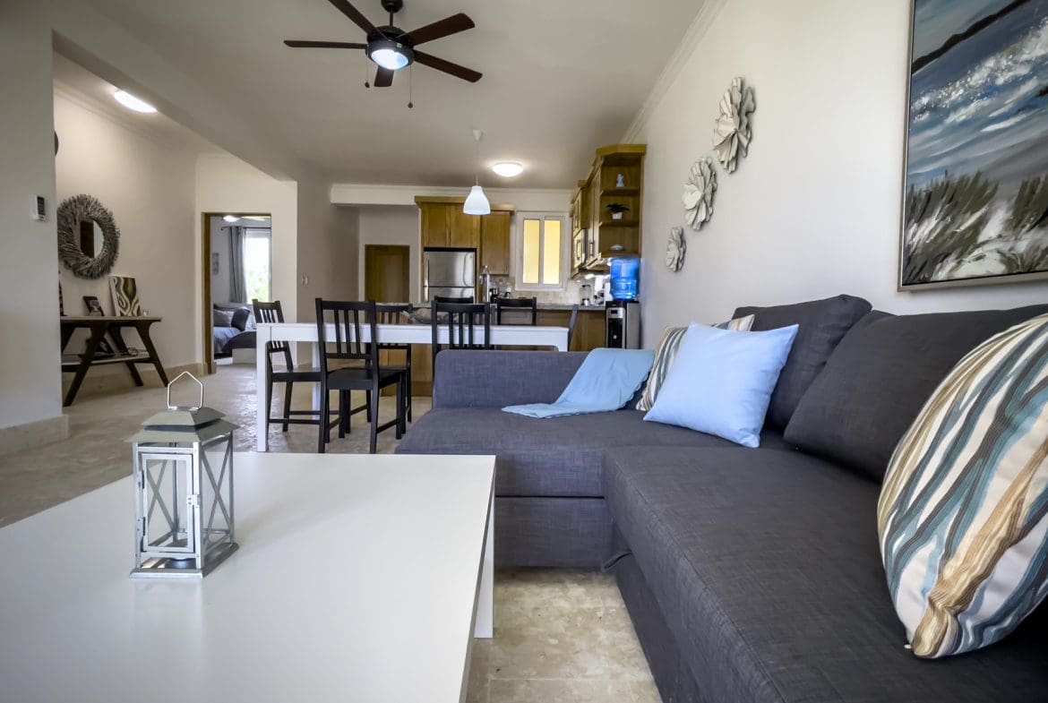 buyDRproperty Living room with gray sectional sofa, white coffee table, and open kitchen in background. Sosua Real Estate