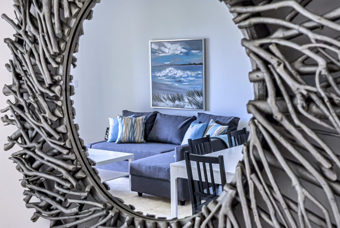 buyDRproperty Cozy living room reflected in driftwood mirror with blue couch and beach painting. Sosua Real Estate