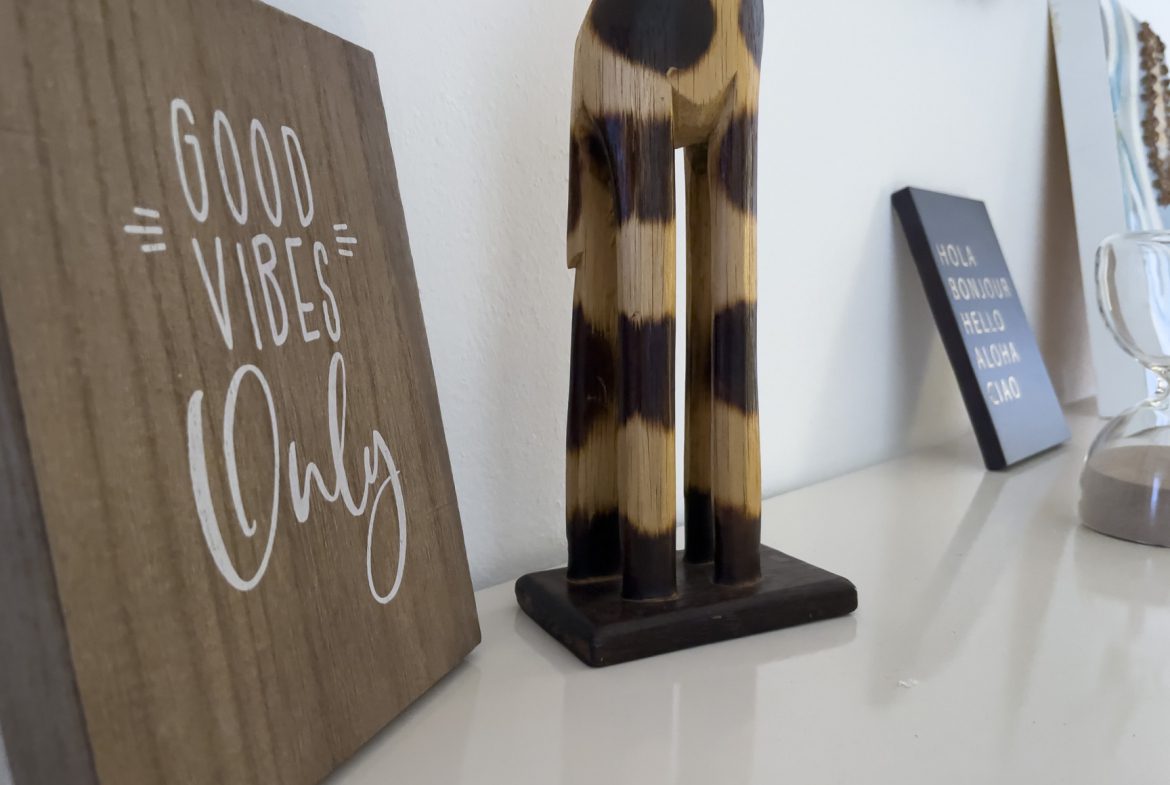 buyDRproperty Good Vibes Only sign, wooden giraffe, and travel-themed decor on a shelf. Sosua Real Estate