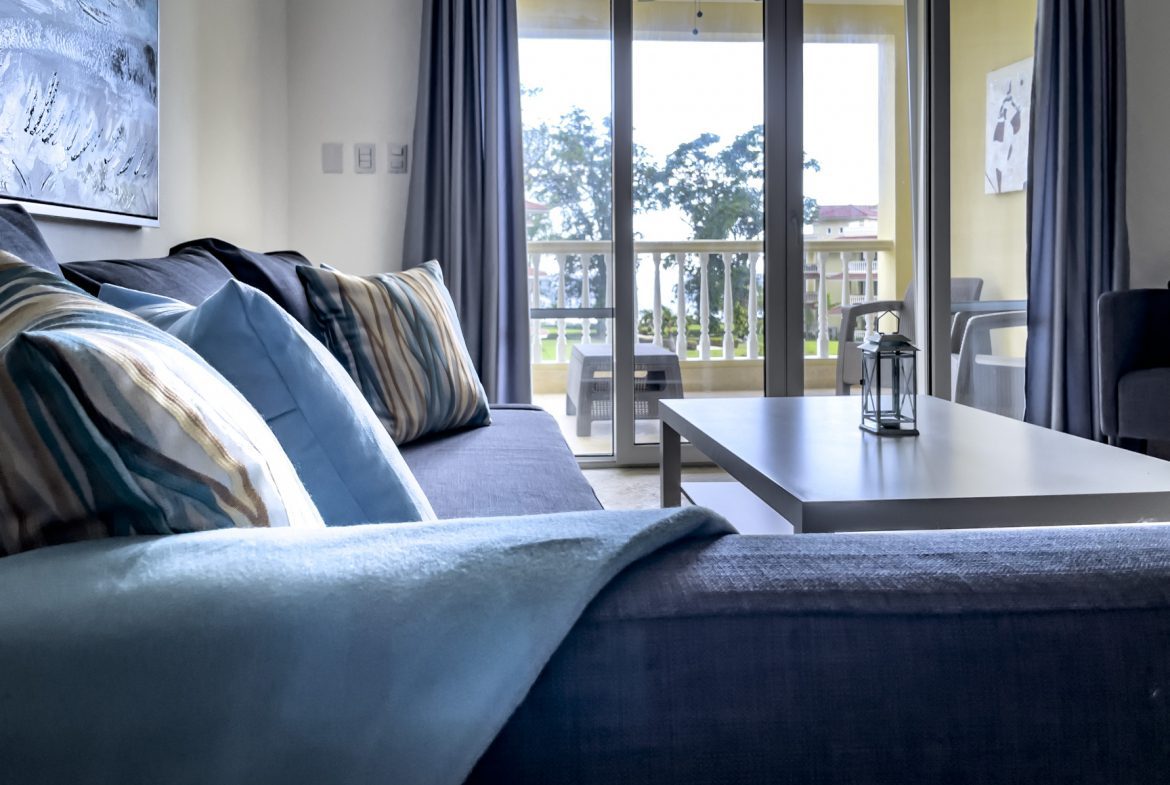 buyDRproperty Living room with blue sofa, pillows, coffee table, and balcony with outdoor furniture. Sosua Real Estate