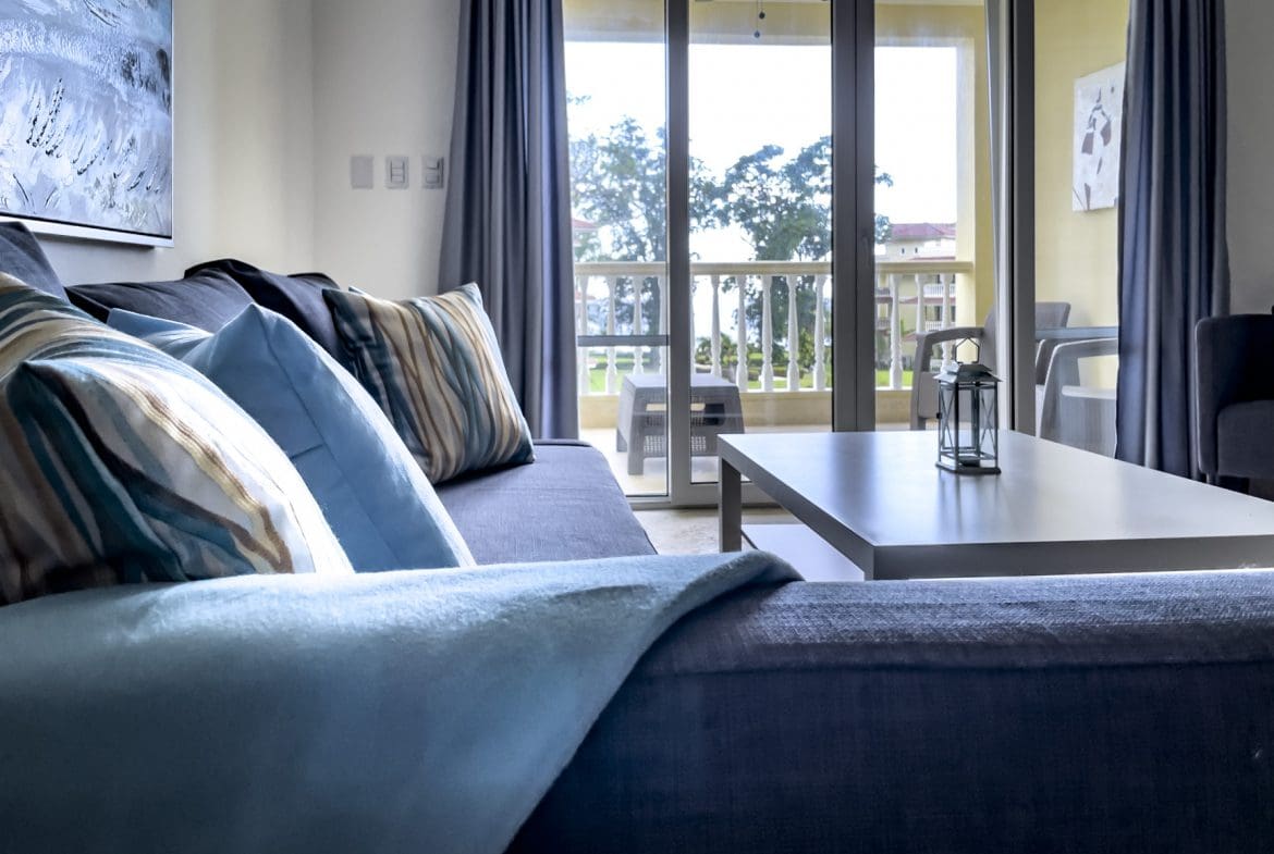 buyDRproperty Living room with blue sofa, pillows, coffee table, and balcony with outdoor furniture. Sosua Real Estate