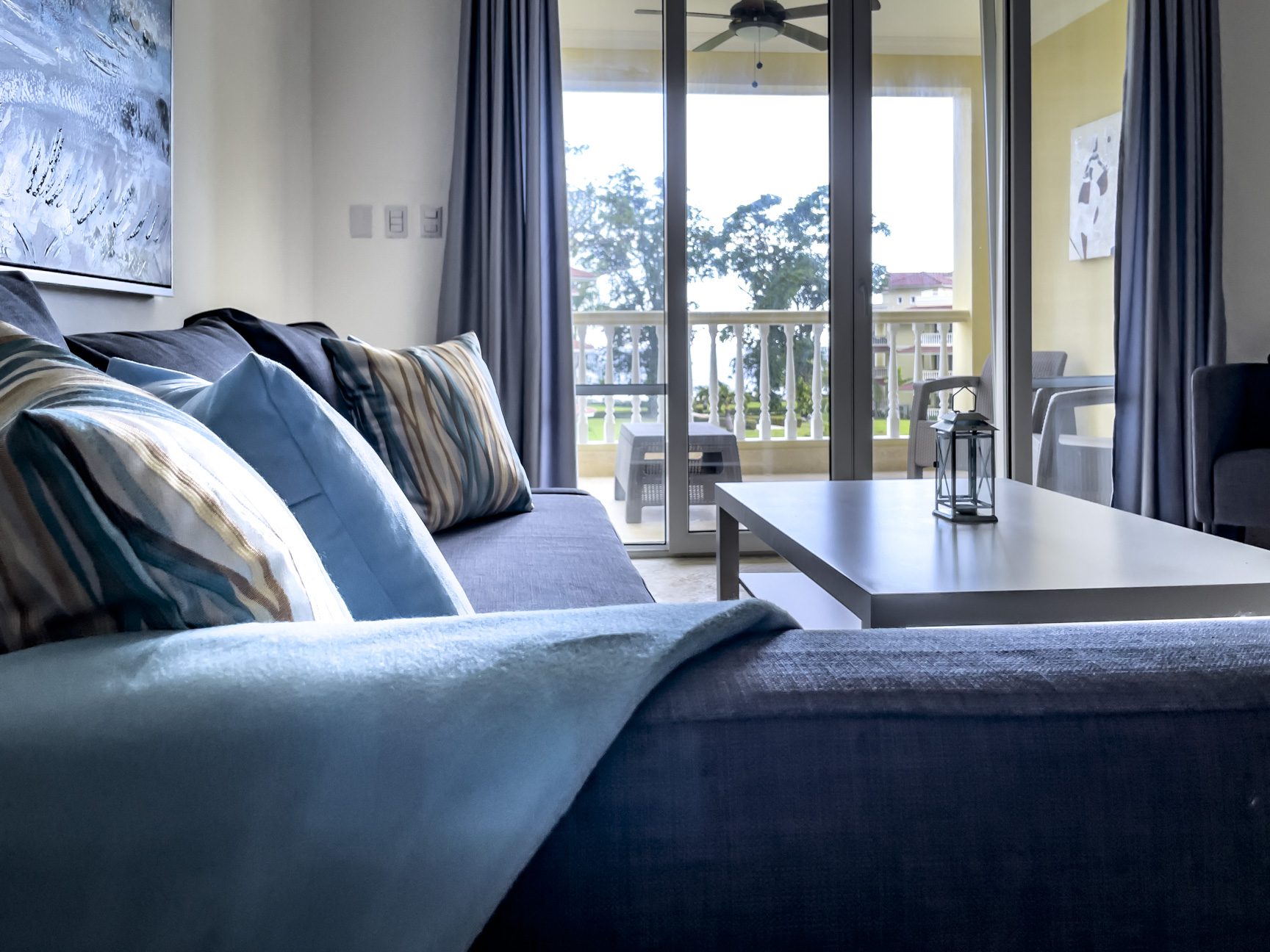 buyDRproperty Living room with blue sofa, pillows, coffee table, and balcony with outdoor furniture. Sosua Real Estate