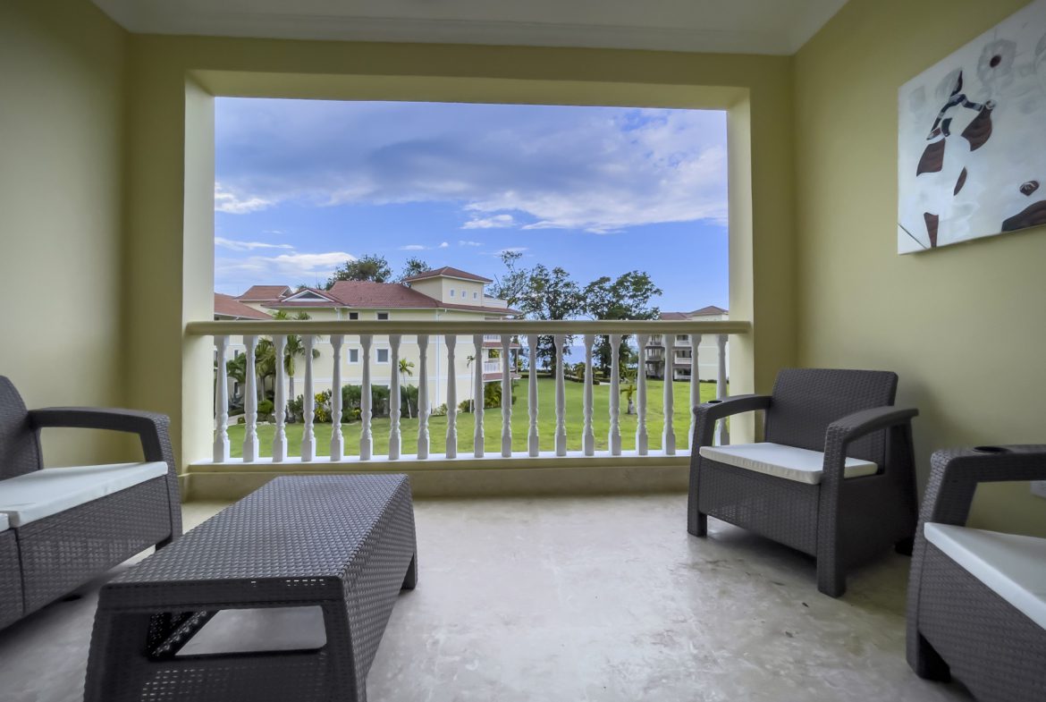 buyDRproperty Balcony with wicker furniture overlooking a resort lawn and buildings. Sosua Real Estate