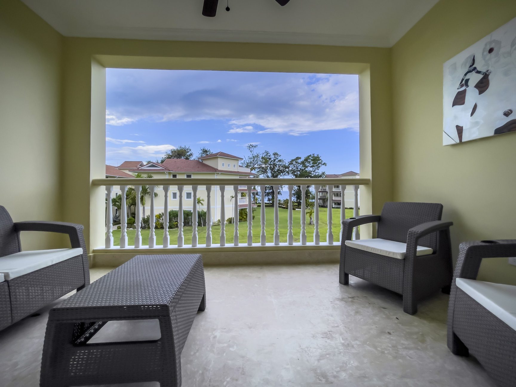 buyDRproperty Balcony with wicker furniture overlooking a resort lawn and buildings. Sosua Real Estate