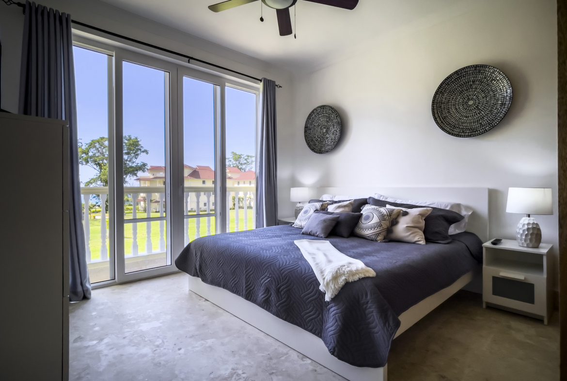 buyDRproperty Bright bedroom with a king bed, balcony, and woven wall art. Sosua Real Estate
