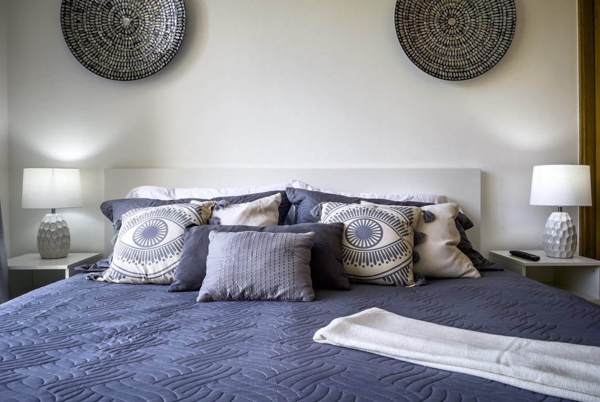 buyDRproperty Cozy bedroom with blue quilt, decorative pillows, and wall art. Sosua Real Estate
