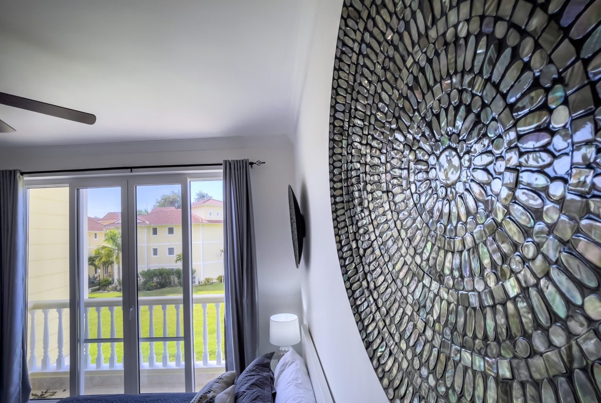 buyDRproperty Bedroom with balcony view, mosaic wall art, and neutral decor. Sosua Real Estate