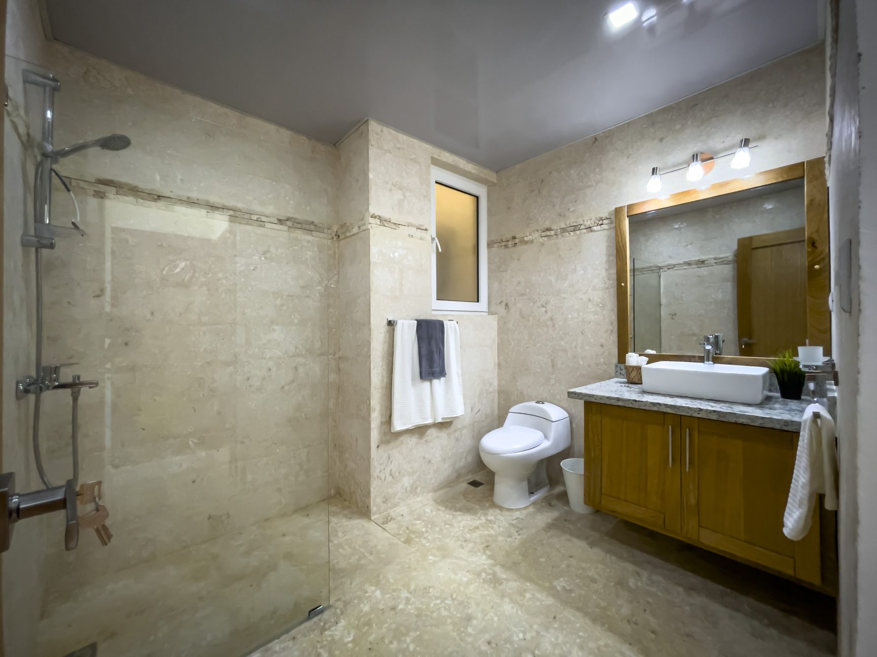 buyDRproperty Bathroom with walk-in shower, toilet, and vanity with wood cabinets and a stone countertop. Sosua Real Estate
