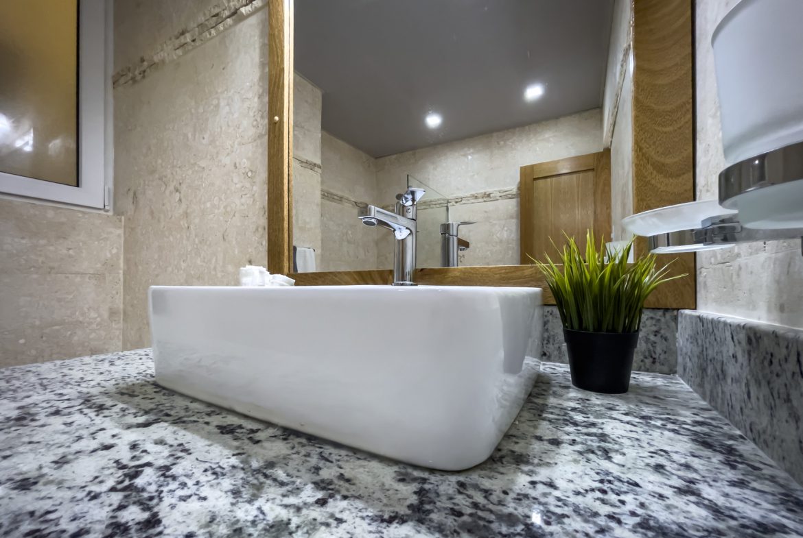 buyDRproperty Modern bathroom with white sink on granite countertop, reflecting in mirror. Sosua Real Estate