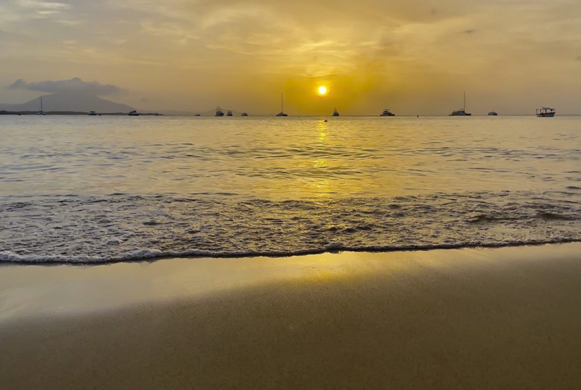 buyDRproperty Golden sunset over the ocean with boats, reflecting on the beach sand and gentle waves. Sosua Real Estate