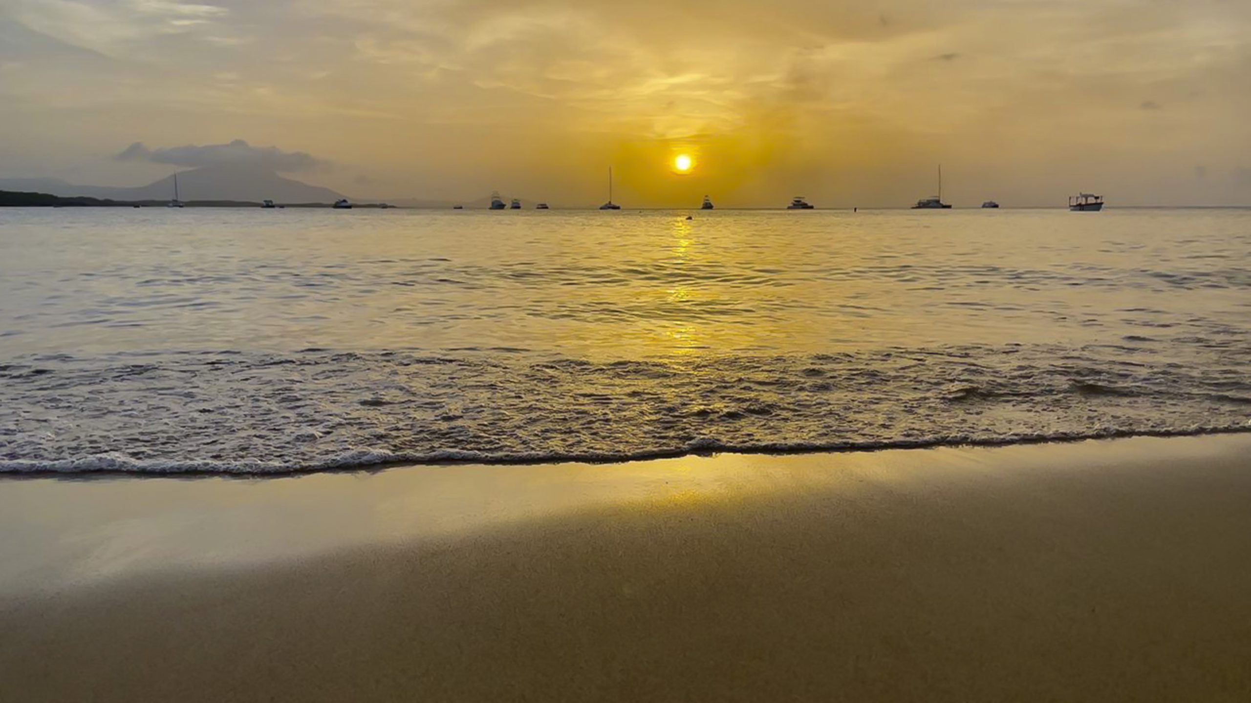 buyDRproperty Golden sunset over the ocean with boats, reflecting on the beach sand and gentle waves. Sosua Real Estate