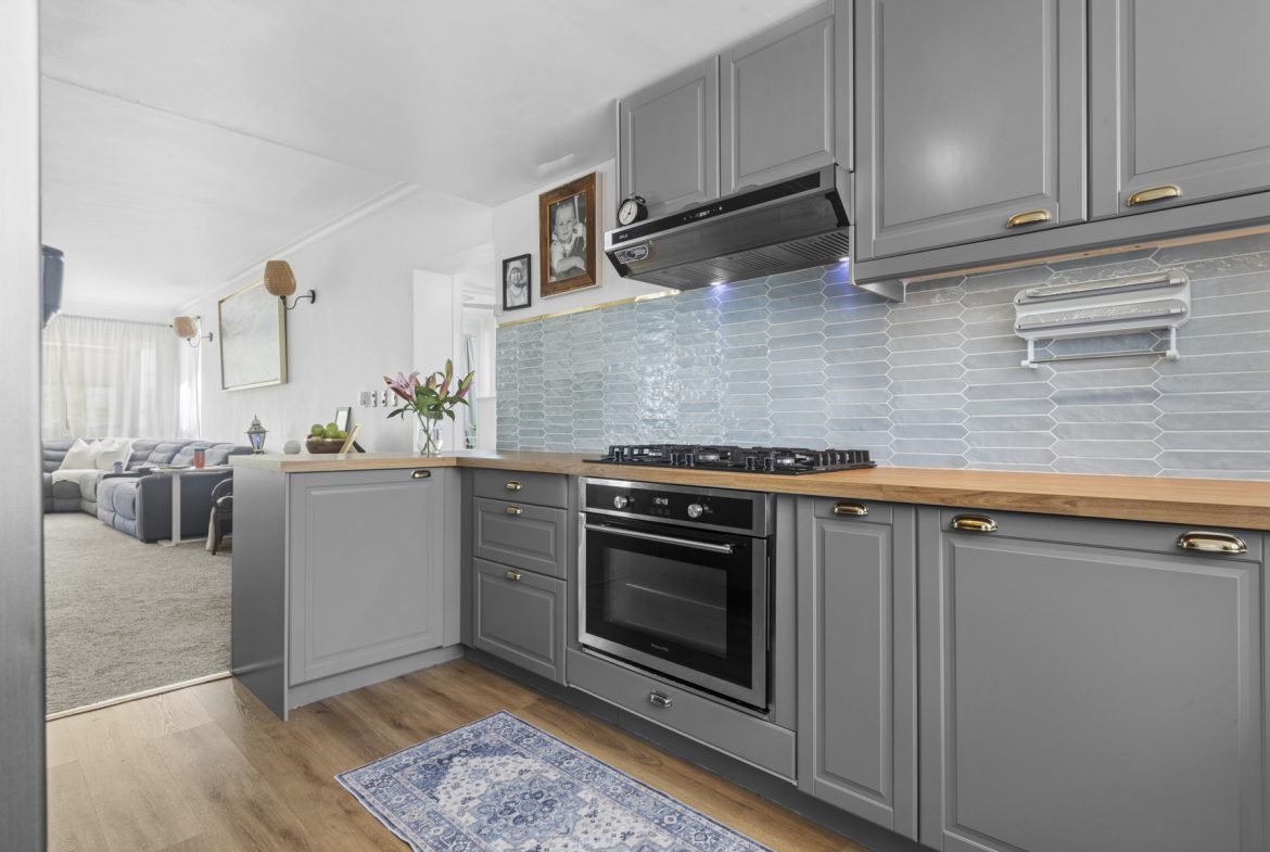 buyDRproperty Modern gray kitchen with wood countertops, blue tile backsplash, and open view into living room. Sosua Real Estate