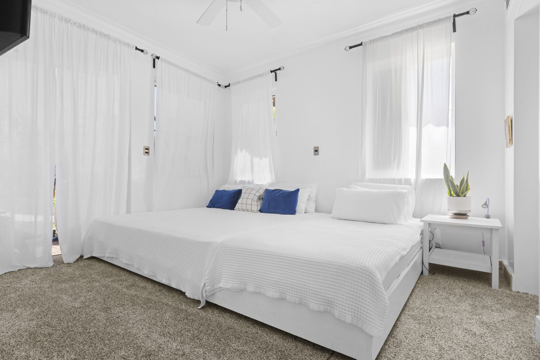 buyDRproperty Bright, minimalist bedroom with a large white bed, sheer curtains, and neutral carpet. Sosua Real Estate