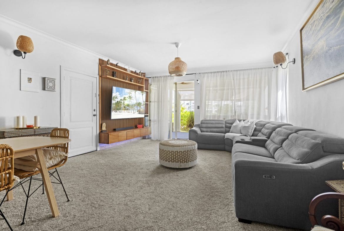 buyDRproperty Bright living room with gray sectional sofa, rattan accents, TV, and neutral carpet. Sosua Real Estate