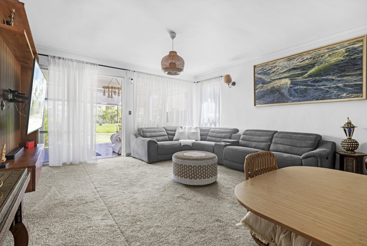 buyDRproperty Cozy living room with gray sectional sofa, woven ottoman, and light-filled patio. Sosua Real Estate