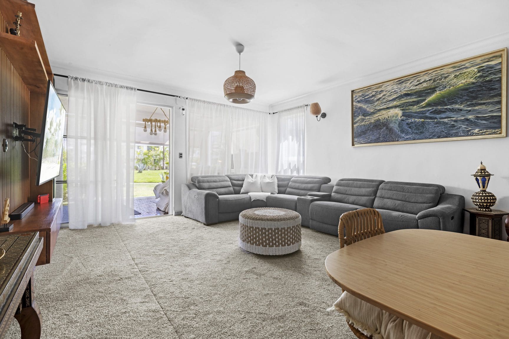 buyDRproperty Cozy living room with gray sectional sofa, woven ottoman, and light-filled patio. Sosua Real Estate